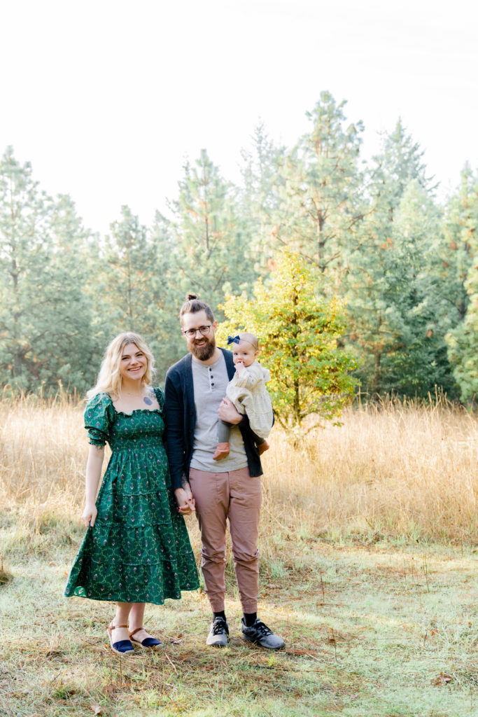 photo of portland oregon family of three standing in a field surrounded by trees with the sun pouring around them