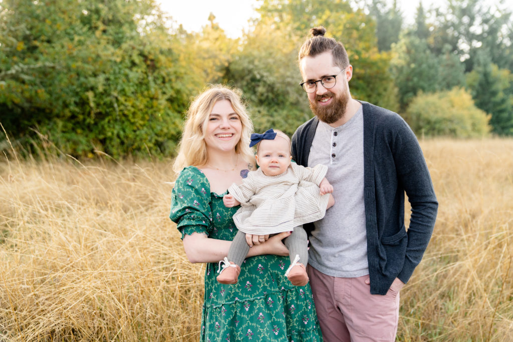 photo of portland oregon family of three standing in a field surrounded by trees with the sun pouring around them