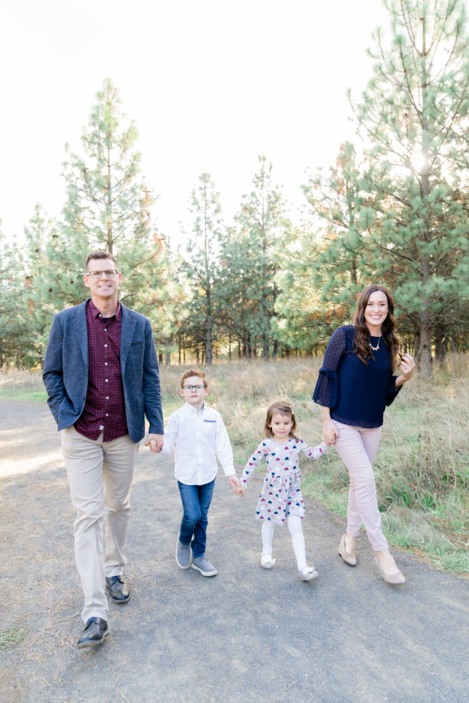 a beautiful oregon family session with ponderosa pine tress and the sun shining through featuring a father, mother, son and daughter walking towards the camera
