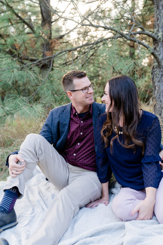 a beautiful oregon family session with ponderosa pine tress and the sun shining through featuring a father and mother smiling at eachother 