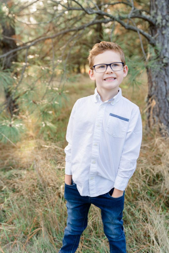 a beautiful oregon family session with ponderosa pine tress and the sun shining through featuring the son smiling at the camera