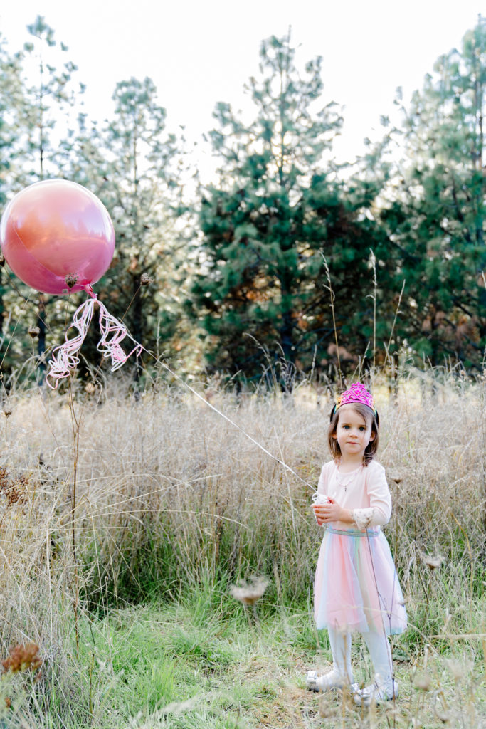 a beautiful oregon family session with ponderosa pine tress and the sun shining through featuring a little girl holding onto a balloon
